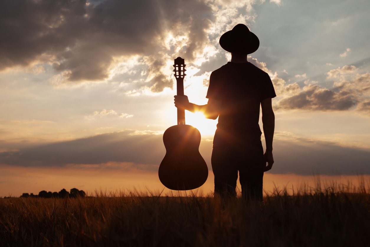 silhouette of musician artist with guitar at sunset, music and creativity background